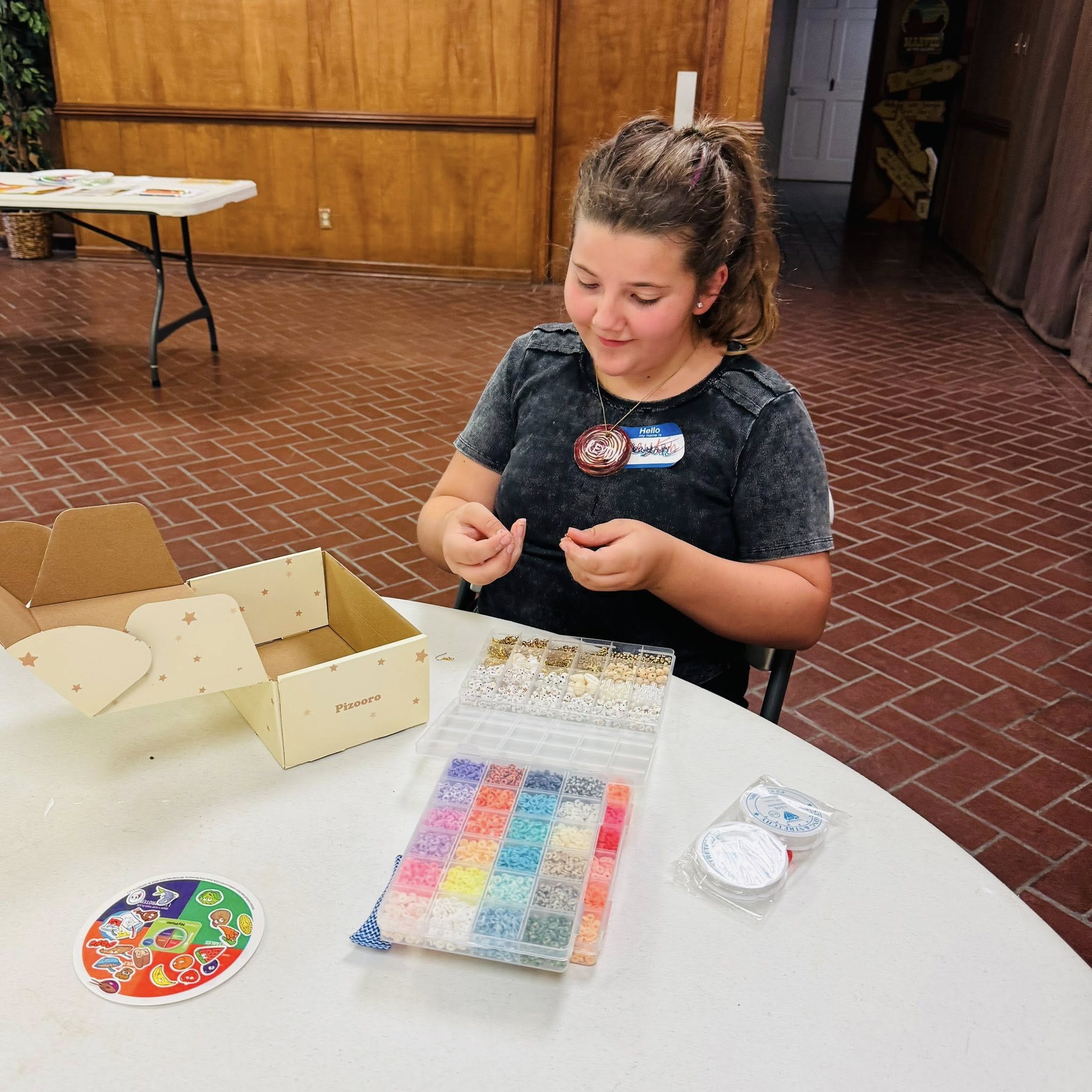 A girl at a table looking at a box of many different colored beads.